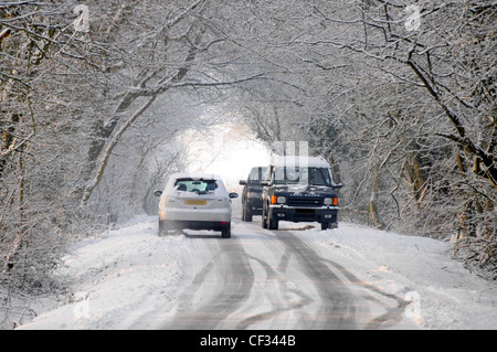 Cars passing on icy snow covered country lane scene (obscured numberplates) Banque D'Images
