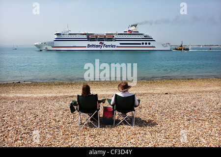 Un couple de chaises portables sur la plage en regardant le ferry quitte le port de Southsea. Banque D'Images