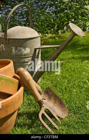 Arrosoir en zinc, truelle, fourchette et pots en argile dans le jardin. Banque D'Images