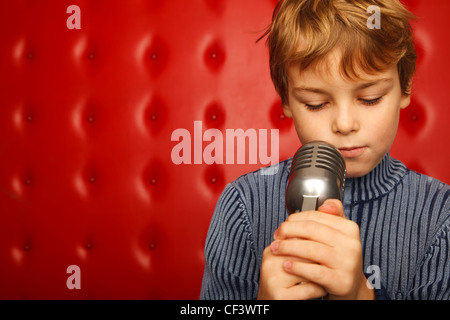 Portrait of boy avec microphone sur crémaillère contre mur rouge. Сlose. Format horizontal. Banque D'Images