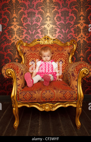 Triste petite fille assise dans le vieux fauteuil. Intérieur en style rétro. Format vertical. Banque D'Images