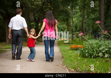 Petite fille en robe rouge de concert avec les parents entre dans le jardin d'été. Girl détient les parents pour les mains. Banque D'Images