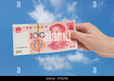 100 yuan chinois un projet de loi avec le portrait de Mao Zedong est tenue à la main. Ciel est dans l'arrière-plan. Banque D'Images