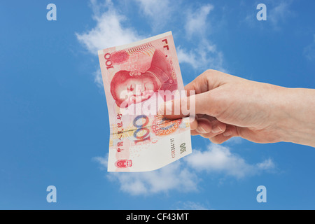 100 yuan chinois un projet de loi avec le portrait de Mao Zedong est tenue à la main. Ciel est dans l'arrière-plan. Banque D'Images