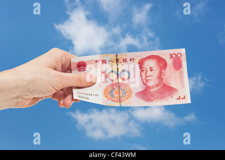 100 yuan chinois un projet de loi avec le portrait de Mao Zedong est tenue à la main. Ciel est dans l'arrière-plan. Banque D'Images