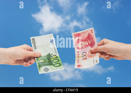 100 yuan chinois un projet de loi est tenue à la main. De l'autre côté une 100 Euro bill est tenue à la main, fond du ciel Banque D'Images