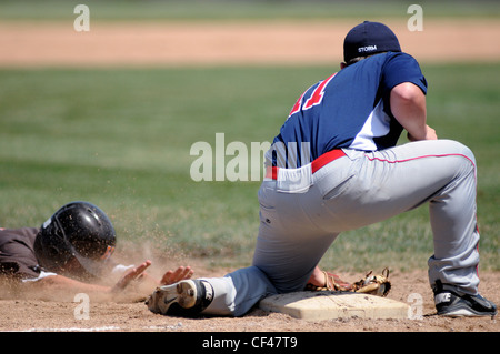 Troisième but balle dans son gant bloque le coureur qui est en train de glisser la tête la première dans la troisième base au cours d'une école d'un match de baseball. Banque D'Images