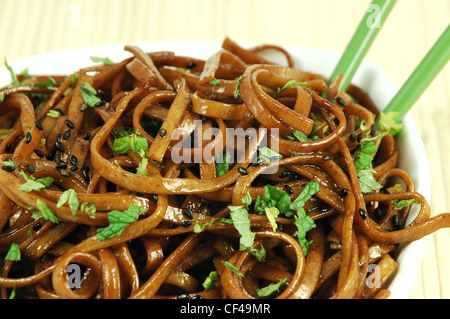 Bol de nouilles Udon sautées garnie de graines de sésame noir et de menthe fraîche avec baguettes vert Banque D'Images