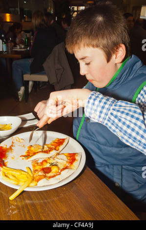 Un garçon de 12 ans de manger une pizza et frites dans un restaurant italien en Angleterre , Angleterre , Royaume-Uni Banque D'Images