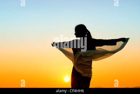 Indian girl with veil tournant dans le vent vers le soleil. Silhouette Banque D'Images