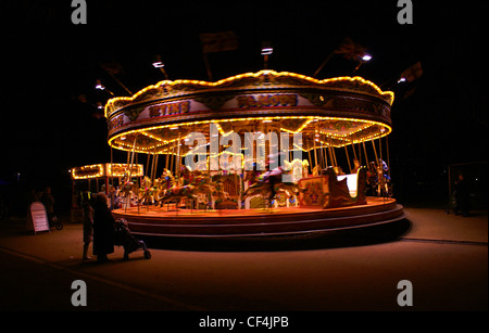 Un comité permanent de la famille par un carrousel de spinning dans Hyde Park la nuit. Banque D'Images