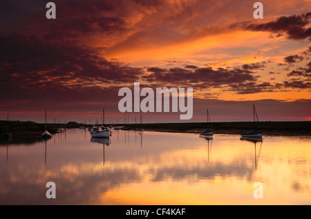 Ciel rouge sur des bateaux amarrés dans le port de Burnham Overy Staithe à Norfolk. Banque D'Images