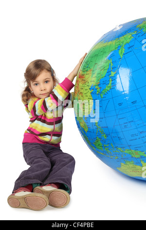 Petite fille assise près de big inflatable globe et le tenant, looking at camera, isolated on white Banque D'Images