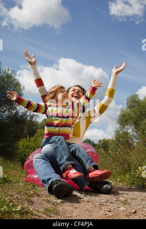 Mère et fille jouer en plein air, assis sur un fauteuil gonflable Haut les mains. Banque D'Images