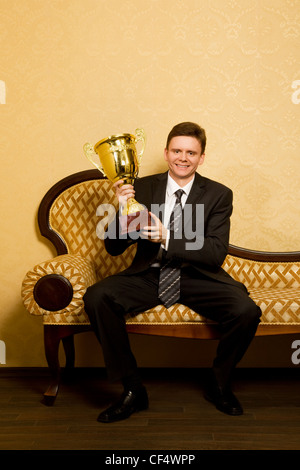 Smiling businessman with win cup dans la main en fonction assis sur un canapé dans la salle à manger Banque D'Images