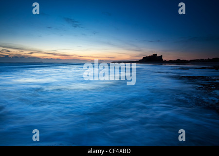 Vue sur la rive vers la silhouette du château de Bamburgh d'ici le début de l'aube lumière. Banque D'Images