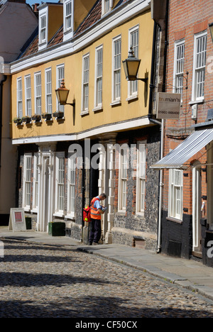 Un postier livrer le courrier à un bien sur Elm Hill, une ruelle pavée historique avec beaucoup de bâtiments datant de la période Tudor Banque D'Images