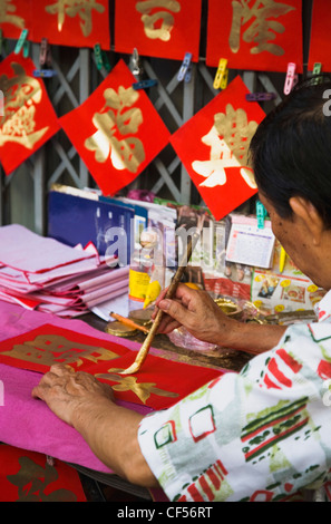 Thaïlande, Bangkok, Chinatown, calligraphe peinture des caractères d'or sur papier rouge, couleurs de bon augure pour le Nouvel An chinois. Banque D'Images