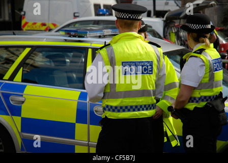 British transport des agents de police de yellow jackets debout à côté d'une voiture de police dans la région de Westminster. Banque D'Images