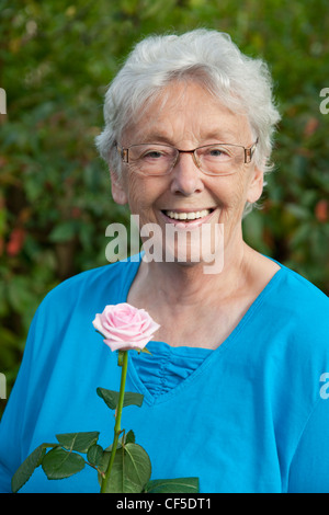 Allemagne, Bavière, Huglfing, Senior woman with rose dans jardin, smiling, portrait Banque D'Images