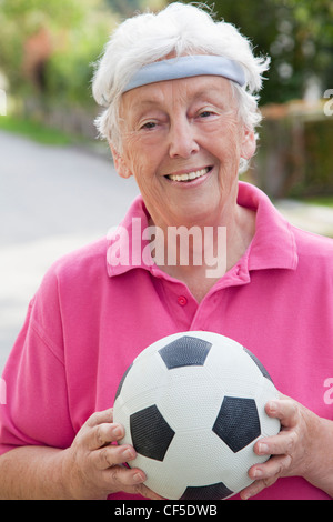 Allemagne, Bavière, Huglfing, Senior woman holding soccer ball, smiling, portrait Banque D'Images