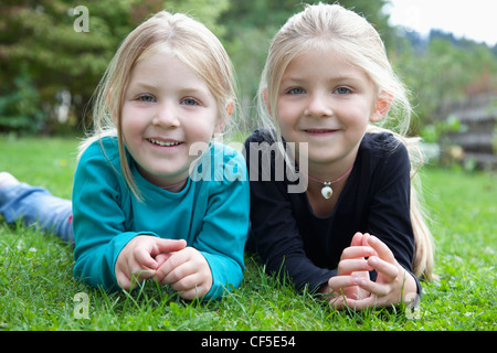 Allemagne, Bavière, Huglfing, Girls lying on grass in garden, smiling, portrait Banque D'Images