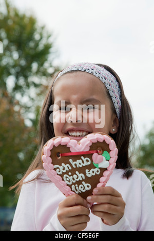 Allemagne, Bavière, Huglfing, Girl holding gingerbread heart in garden, smiling, portrait Banque D'Images