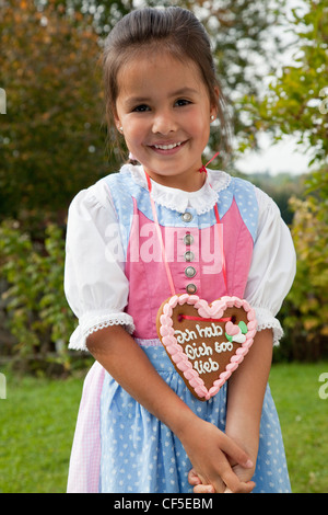 Allemagne, Bavière, Huglfing, Girl with gingerbread heart in garden, smiling, portrait Banque D'Images