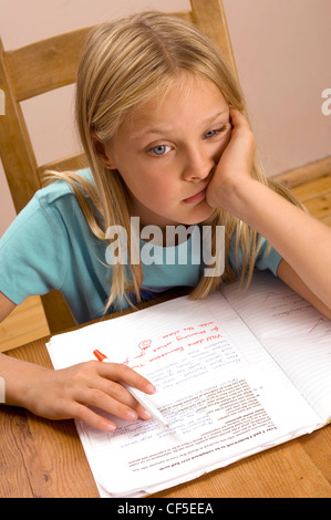Enfant de sexe féminin était assis à une table en bois à faire leurs devoirs, s'appuyant sa tête sur sa main Banque D'Images
