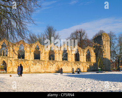 Les gens qui marchent dans la neige dans le Yorkshire Museum Gardens par les ruines de l'abbaye de St Mary's Church. Banque D'Images