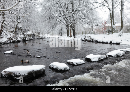 Stepping Stones recouvert de neige menant à travers une rivière. Banque D'Images