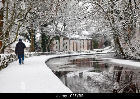 Un homme qui marche le long d'un halage couvert de neige par l'Huddersfield canal étroit. Banque D'Images