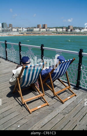 Deux personnes âgées s'asseoir dans des chaises longues sur la jetée de Brighton. Banque D'Images