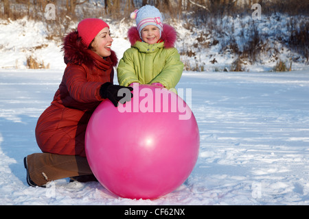 Mère et fille jouer dehors en hiver, avec de gros ballon gonflable. Banque D'Images