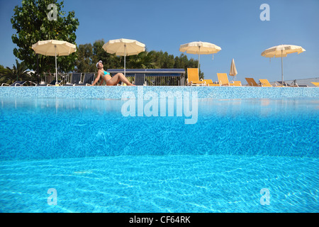Femme devient bronzé près de la piscine sous un ciel-ouvert en journée, près de chaises-longues et parasols, la moitié sous l'eau photo Banque D'Images