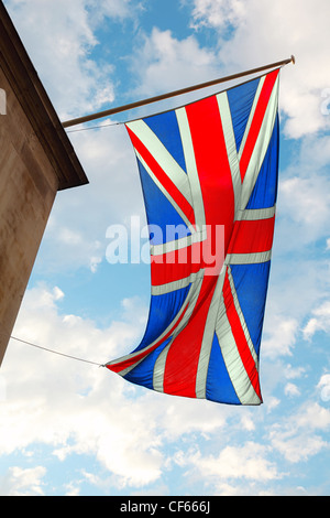 Brandir le drapeau britannique dans le vent. en arrière-plan de ciel bleu avec des nuages blancs Banque D'Images