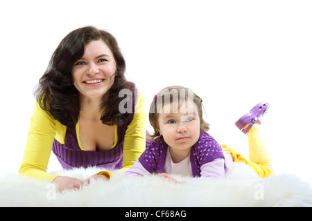 Heureux mère dans les vêtements clairs et rire petite fille sur la fourrure blanche jusqu'à Banque D'Images