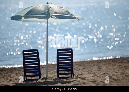 Deux chaises vides bleu foncé se tenir sur la mer près de la plage à l'ombre du grand parasol Banque D'Images