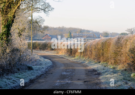 Une allée bordée d'arbustes couverts de givre et verges avec des bâtiments de ferme visible à l'extrémité de la ruelle.des scènes d'hiver à Wooburn Moor Banque D'Images