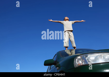 Boy stands sur la tête de voiture largement plaçant les mains et poussa jusqu'face vers le haut sur sky Banque D'Images