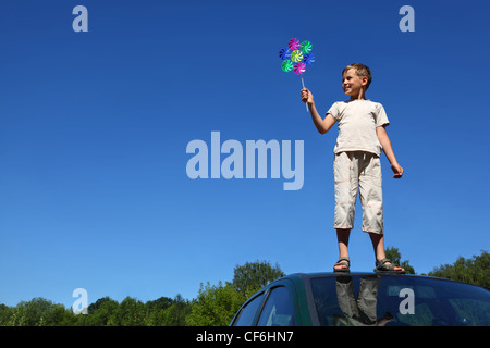 Boy stands sur toit de voiture et tient en main moulin Banque D'Images