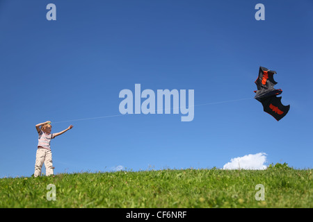 Garçon en été se tient sur l'herbe et commence le kite en forme flittermouse Banque D'Images