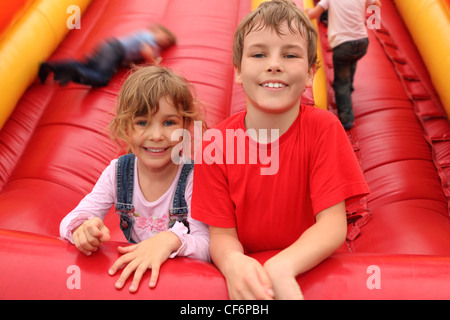 Little Boy and girl lying on red inflatable slide, smiling and looking at camera Banque D'Images