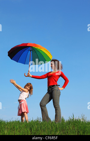 Mère se dresse sur l'herbe verte sur le terrain contre le ciel bleu holding umbrella colorés sur sa fille qui est debout à côté d'elle Banque D'Images