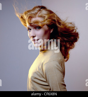 Couleurs de cheveux ondulés cheveux longs femme brune d'être soufflé par la mèche de cheveux de la machine du vent à travers le front, portant polo beige Banque D'Images