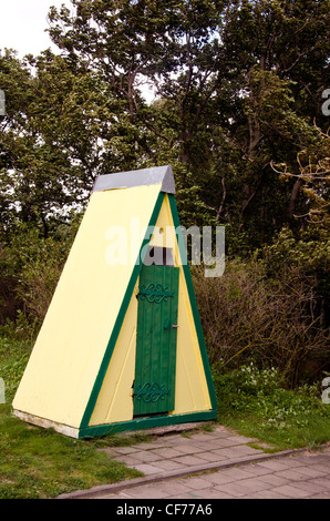 Wc toilettes décoratifs d'extérieur près de parc arbres. Mur de brique jaune vert avec porte en bois. Banque D'Images