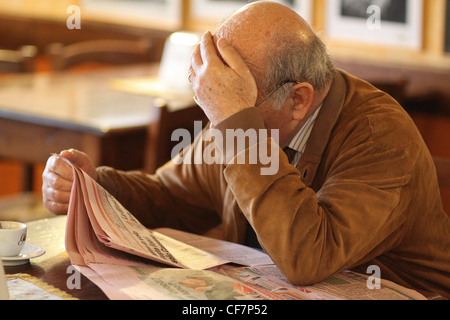 Un vieillard assis dans un bar local de lire les journaux. San Daniele del Friuli, Italie. Banque D'Images