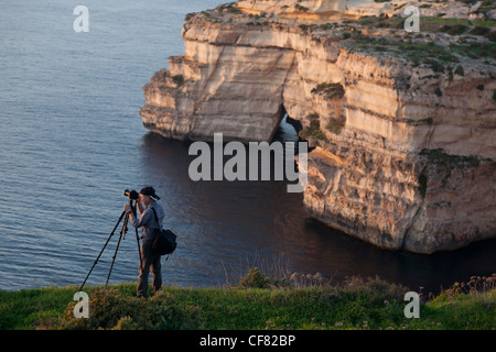 Un photographe à prendre des photos de paysages de falaise et le coucher du soleil sur la falaise près de Xlandi sur la côte sud de l'île de Gozo. Banque D'Images