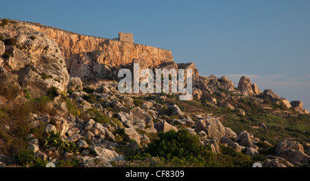 Une tour de guet côtière médiévale se distingue en haut d'une falaise qui pèse sur ski entourée de rochers dans la côte nord de Gozo. Banque D'Images