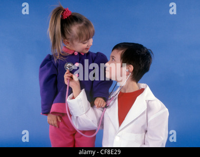 Un jeune garçon se fait passer pour un médecin et écoute le coeur d'une petite fille patient à l'aide d'un stéthoscope. Banque D'Images